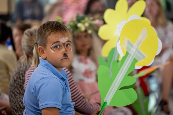 Ein Junge mit Tier-Gesichtsbemalung blickt während der Theateraufführung „Das magische Buch“ in die Kamera, neben ihm eine große gelbe Papierblume.