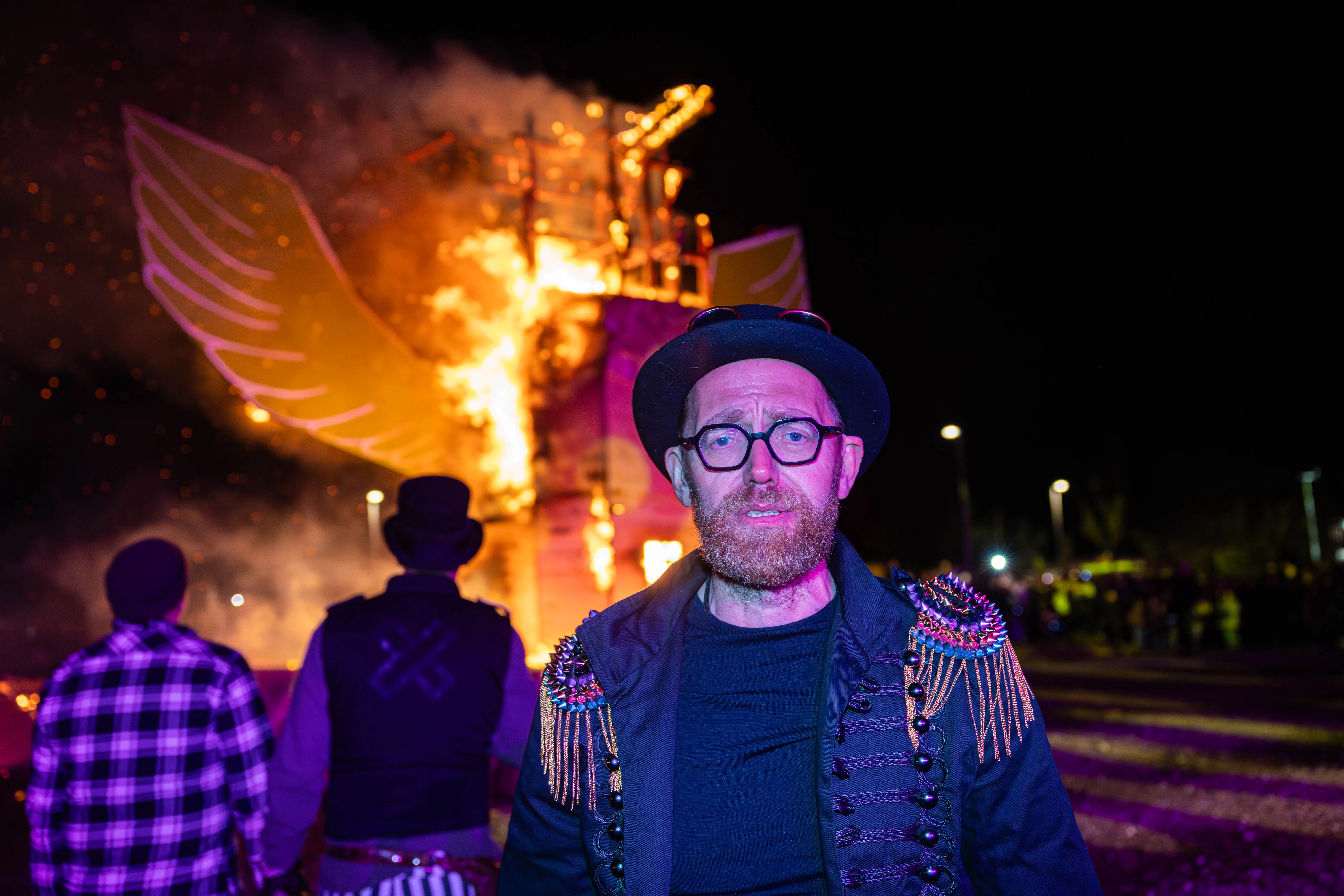 Mann mit Bart und Brille vor brennender Holzkonstruktion mit Flügelmotiven bei einer Osterfeuer-Veranstaltung in Lüdenscheid.