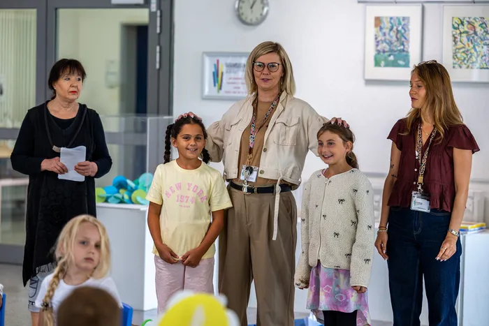 Eine Frau in beiger Kleidung legt ihre Hände auf die Köpfe zweier lächelnder Mädchen, während zwei weitere Frauen neben ihnen stehen.