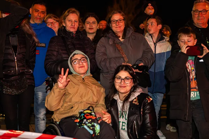 Menschengruppe vor dunklem Hintergrund, einige zeigen Friedenszeichen. Im Vordergrund eine Frau im Rollstuhl und eine junge Frau mit Brille.