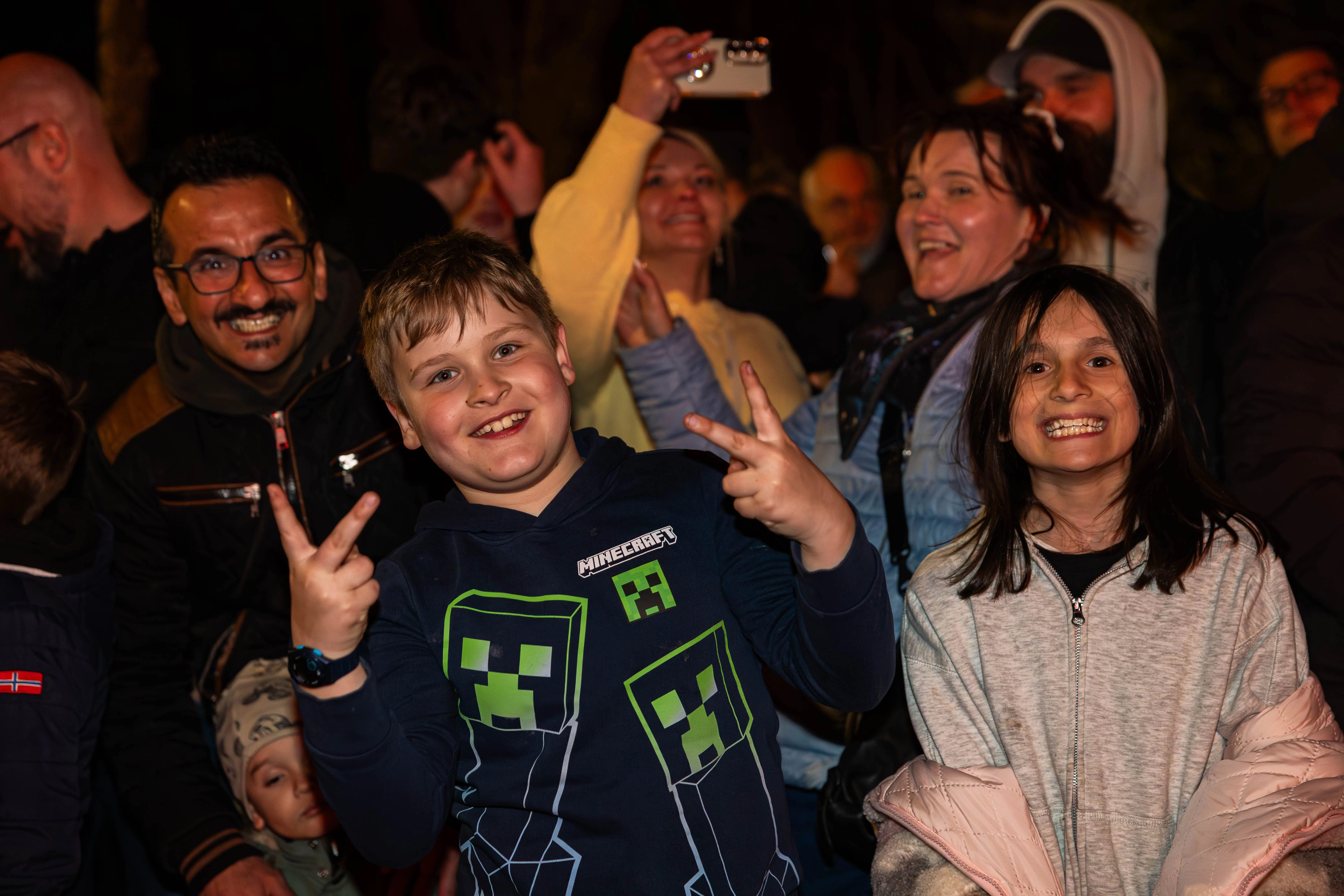 Junge mit Minecraft-Kapuzenpulli zeigt Victory-Zeichen vor jubelnder Menschenmenge bei Osterfeuer in Lüdenscheid.
