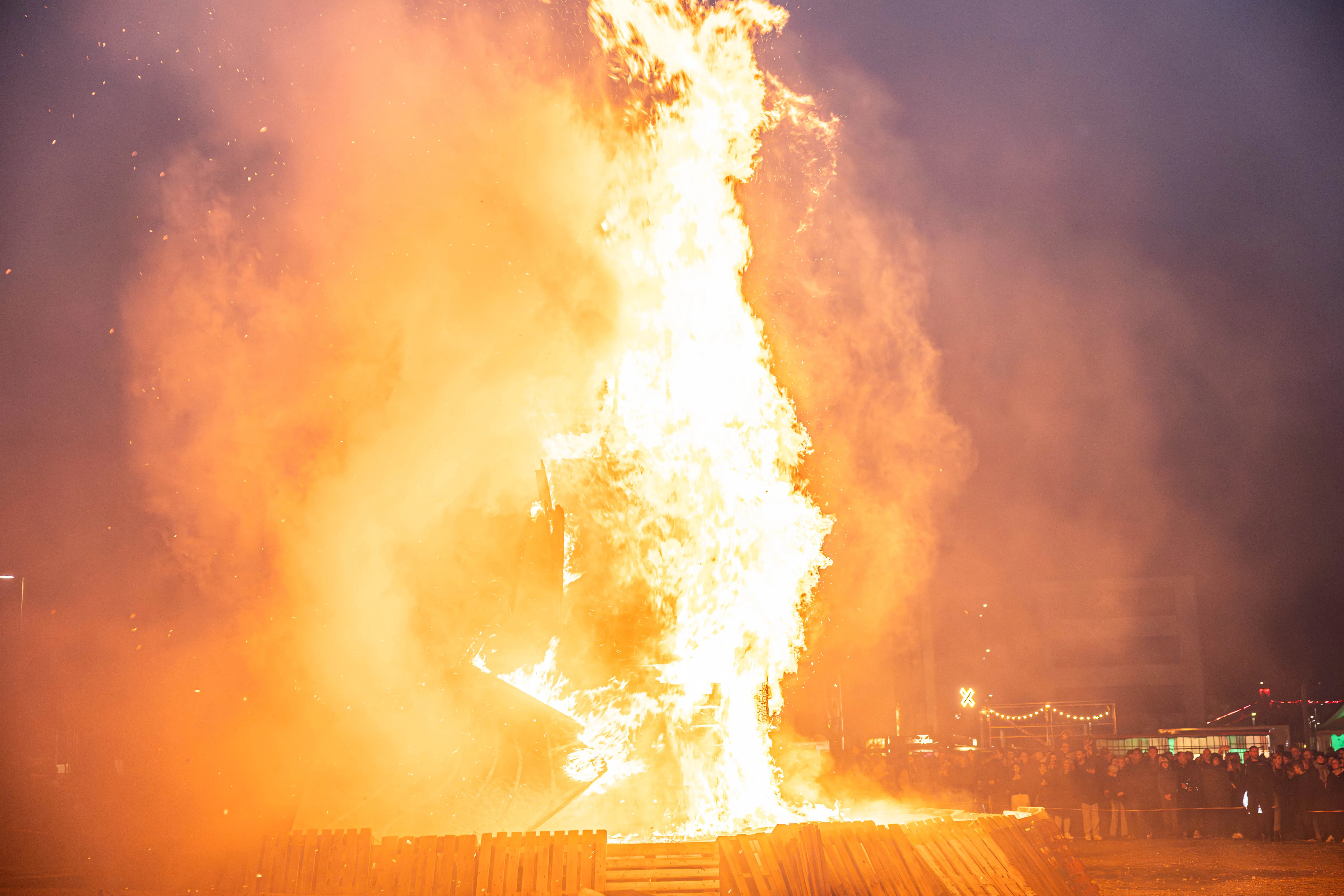 Hohes Osterfeuer mit lodernden Flammen und Funkenflug vor einer Menschenmenge in der Dunkelheit.
