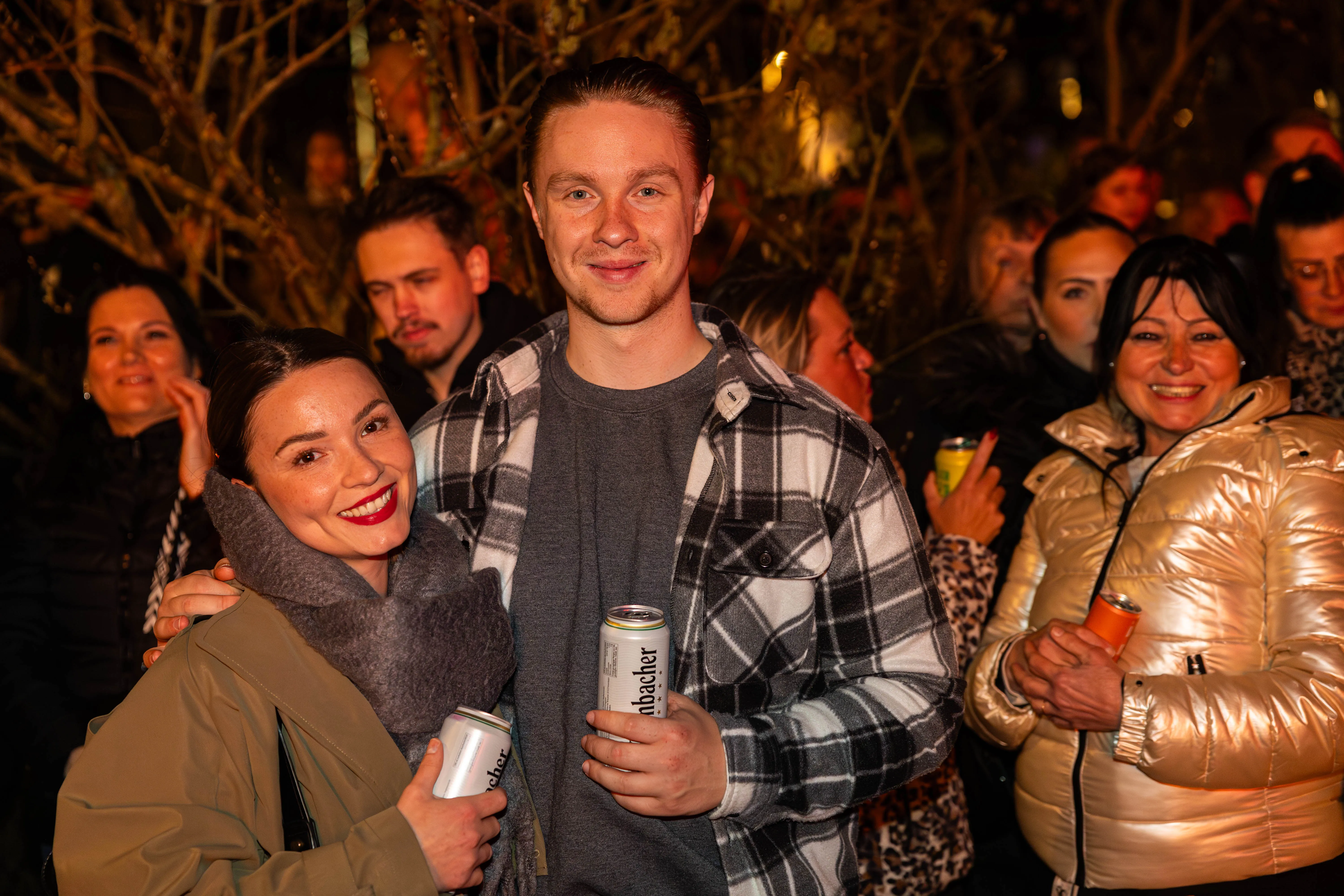 Zwei lächelnde junge Erwachsene im Vordergrund, umgeben von einer Menschenmenge bei einer Osterfeuer-Veranstaltung in Lüdenscheid.