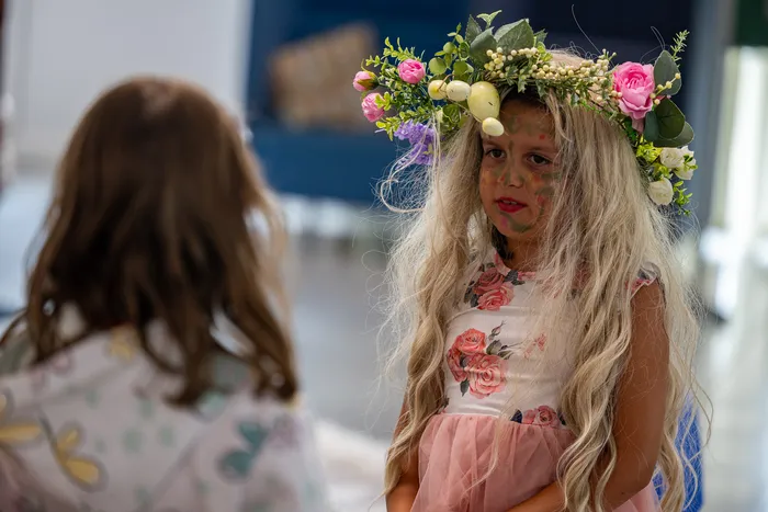Ein Mädchen mit langem blondem Haar, einem Blumenkranz und Gesichtsbemalung trägt ein Kleid mit Rosenmuster.
