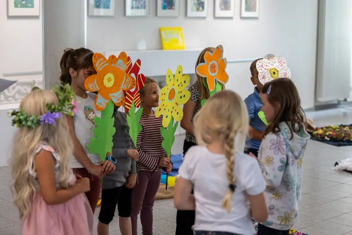 Kinder halten große, bunte, selbstgemachte Papierblumen auf Stielen während einer Theateraufführung.