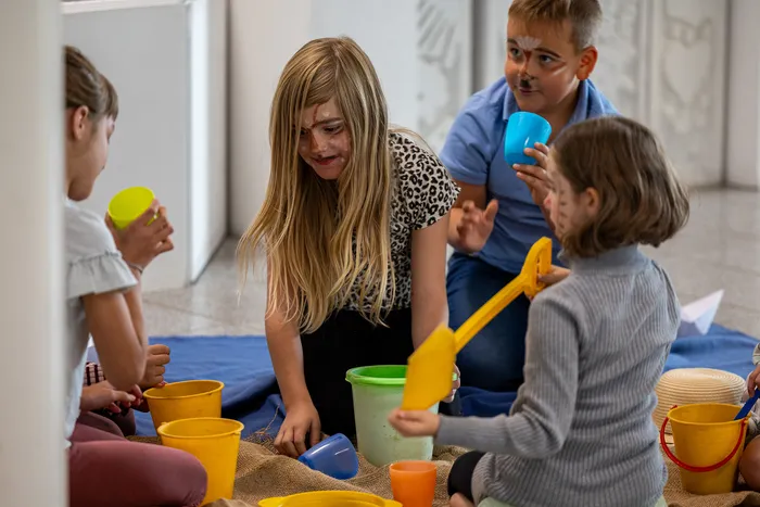 Kinder mit Gesichtsbemalung spielen mit bunten Eimern und Spielzeug auf dem Boden.