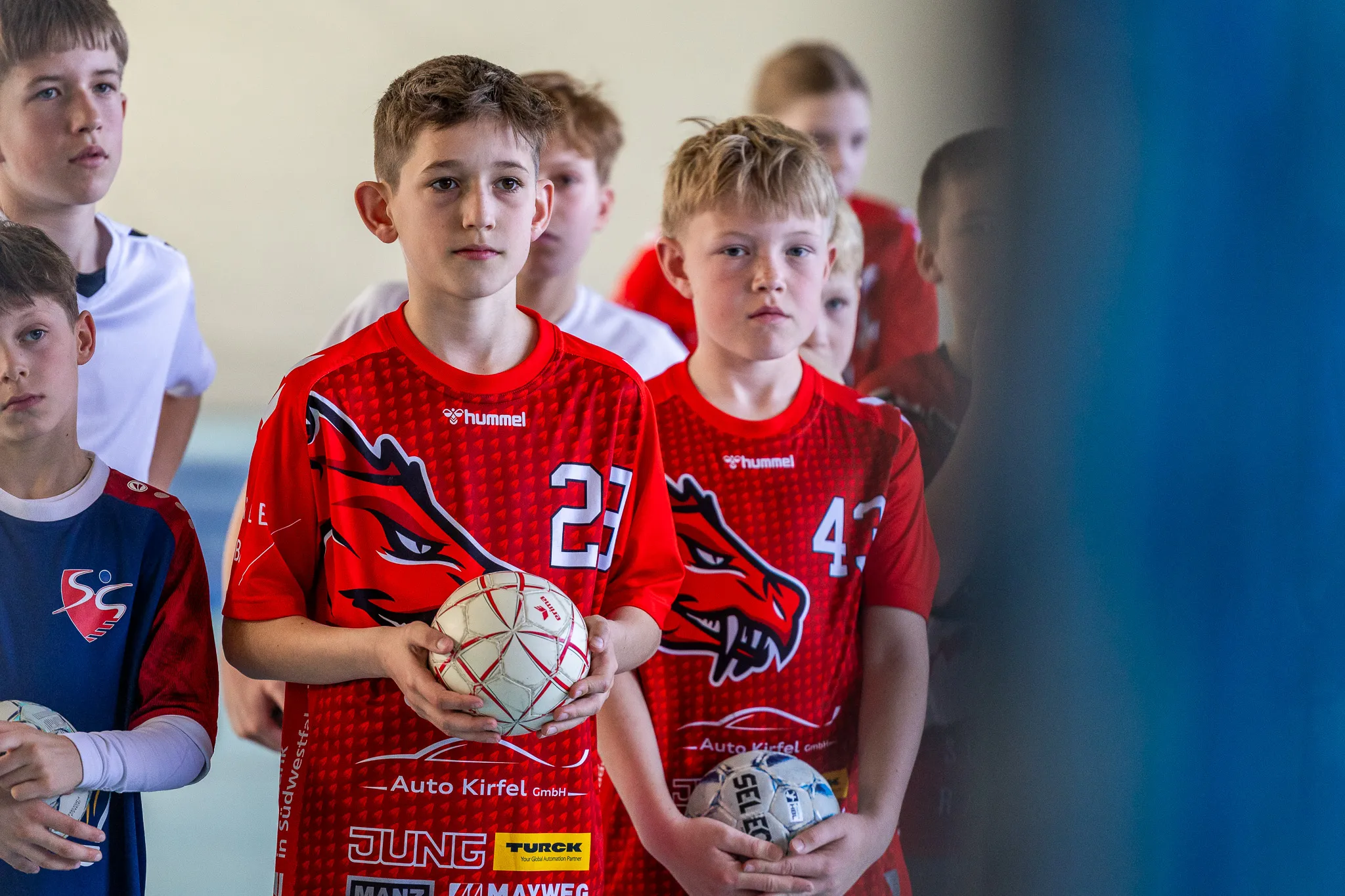 Vier Jungen im Handballtrikot mit Drachenmotiv stehen nebeneinander und schauen konzentriert in die Kamera. Einer hält einen Handball.