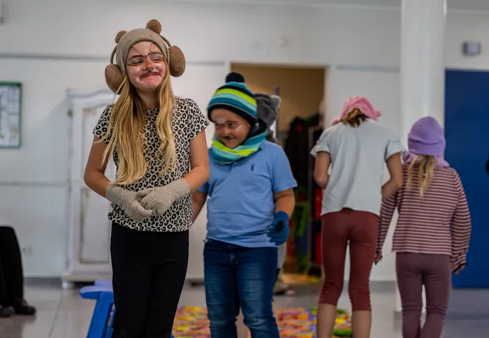 Kinder mit Gesichtsbemalung und Kostümen, darunter ein Mädchen mit Bärenmütze und Leopardenmuster-Shirt, führen ein Theaterstück auf.