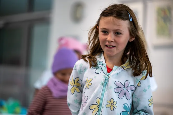 Ein lächelndes Mädchen mit braunen Haaren trägt einen hellblauen Kapuzenpullover mit großen bunten Blumen.