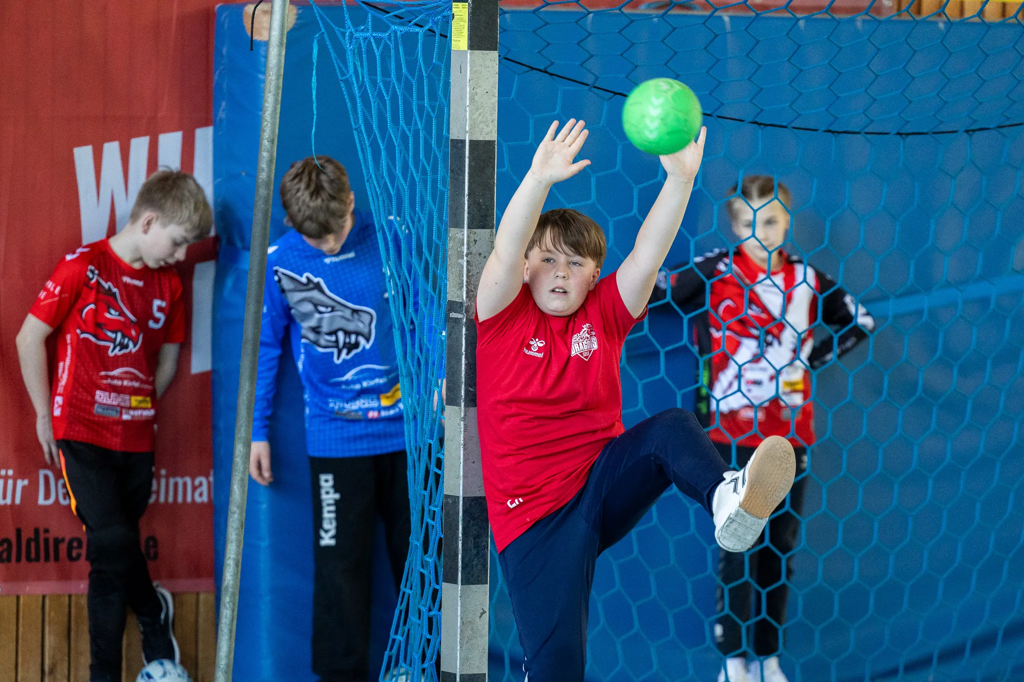 Junge im roten Trikot springt beim Handball-Ostercamp der SGSH Dragons hoch, um einen Ball abzuwehren.