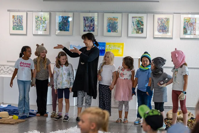 Kinder in Kostümen und eine Frau stehen auf einer Bühne während der Aufführung des Theaterstücks „Das magische Buch“.