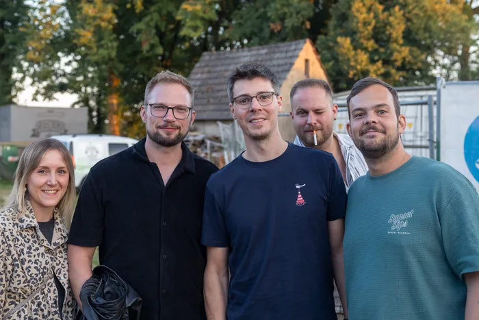Fünf lächelnde Personen posieren für ein Gruppenfoto bei der Q-Stall-Party im Freien.