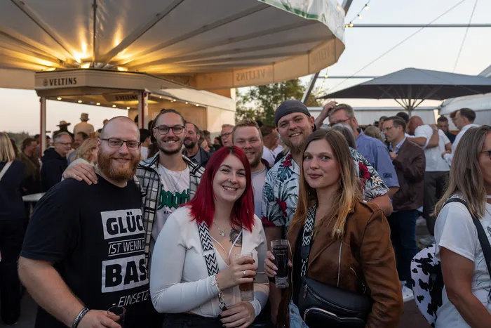 Eine Gruppe lächelnder Menschen posiert bei einer Abendveranstaltung unter einem weißen Zeltdach.