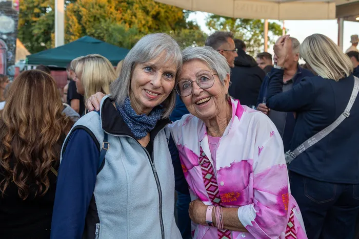 Zwei lächelnde Frauen stehen eng beieinander vor einer Menschenmenge bei der zehnten Q-Stall-Party in Schalksmühle.