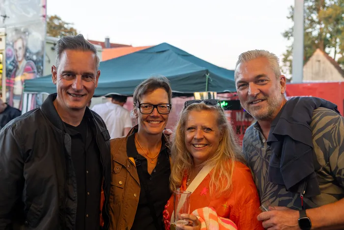 Vier lächelnde Gäste posieren bei der zehnten Q-Stall-Party in Schalksmühle vor einem grünen Zelt.