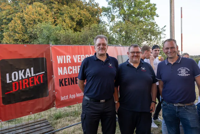 Drei Männer stehen vor einem roten Banner mit der Aufschrift „LOKAL_DIREKT“ bei der Q-Stall-Party in Schalksmühle.