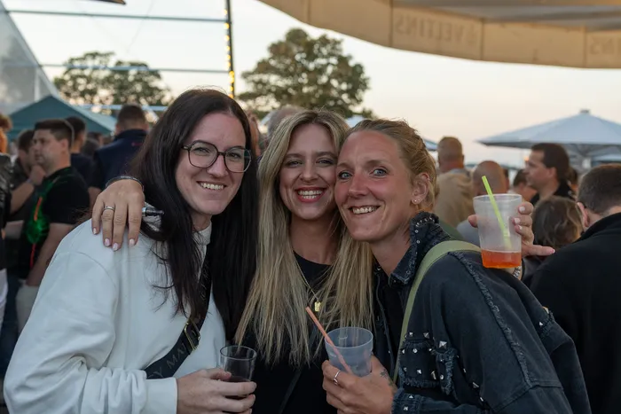 Drei lächelnde Frauen posieren bei der zehnten Q-Stall-Party in Schalksmühle. Eine von ihnen hält einen Becher mit einem orangefarbenen Getränk.