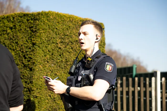 Ein Polizist in Uniform mit kugelsicherer Weste spricht in ein Funkgerät, während er Notizen in einen Block schreibt.