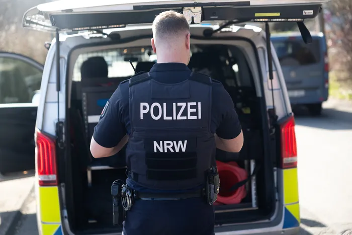 Polizist mit der Aufschrift „POLIZEI NRW“ auf seiner Schutzweste steht vor einem geöffneten Transporter.