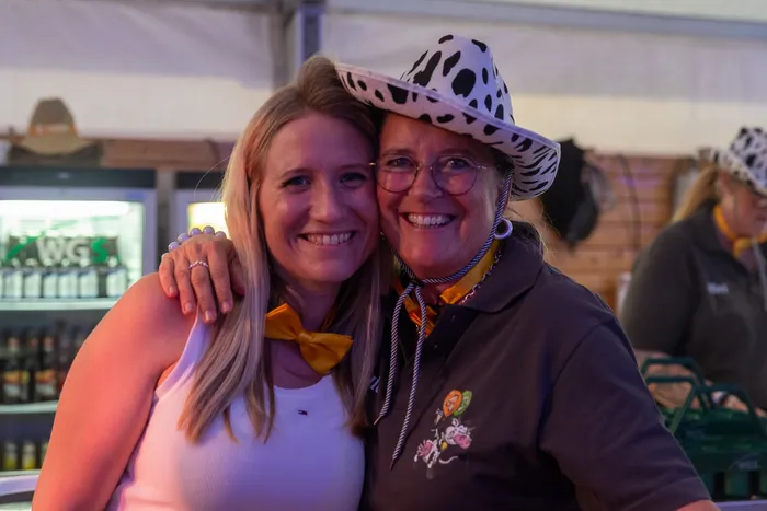 Zwei lächelnde Frauen umarmen sich bei der Q-Stall-Party in Schalksmühle. Eine trägt einen Hut mit Kuhmuster.
