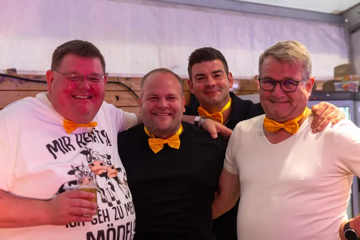 Vier lächelnde Männer mit gelben Fliegen posieren bei der zehnten Q-Stall-Party in Schalksmühle.