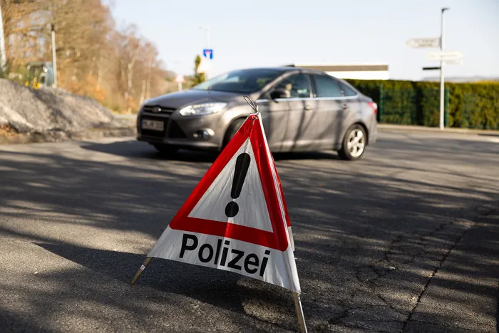 Rotes Warndreieck mit dem Aufdruck „Polizei“ steht auf einer Straße vor einem grauen Auto.