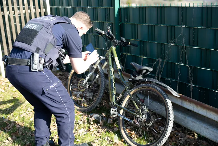 Ein Polizist in Uniform notiert Daten von einem Mountainbike in ein Handgerät. Im Hintergrund ein Maschendrahtzaun.