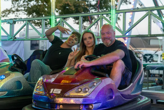 Ein bärtiger Mann, eine junge Frau und ein junger Mann posieren in Bumper Cars auf der Q-Stall-Party in Schalksmühle.