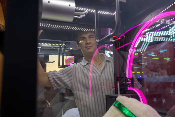Ein junger Mann blickt durch eine Glasscheibe vor pinkfarbenen Neonlichtern.
