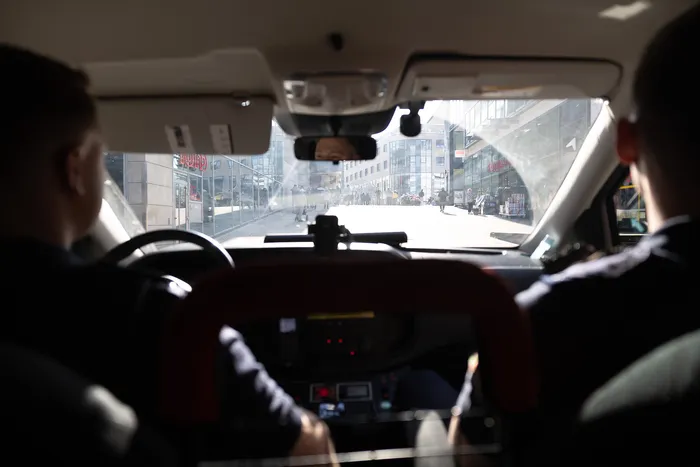 Aus der Perspektive des Fahrers im Cockpit eines Streifenwagens Blick auf eine Straße mit Fußgängern und Gebäuden.
