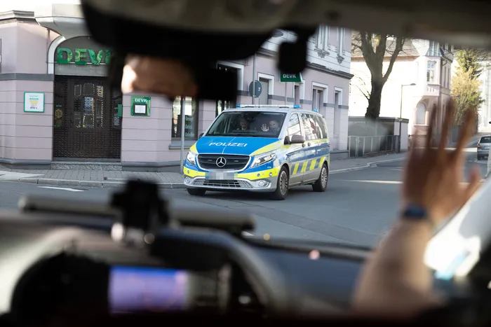 Polizeiwagen fährt auf einer Straße vor einer Bank vorbei, fotografiert durch mehrere Handys.