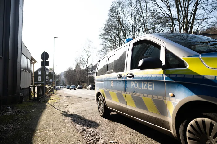 Polizeiwagen steht am Straßenrand, Blaulicht ist aktiviert. Im Hintergrund sind weitere Fahrzeuge und Bäume zu sehen.