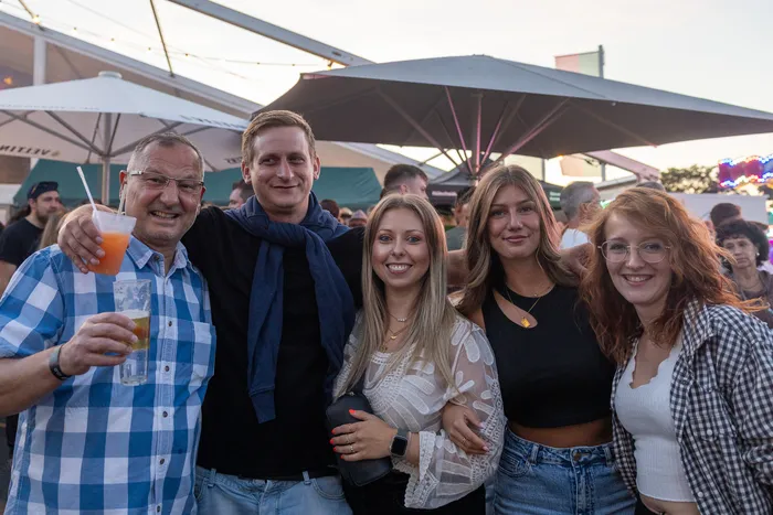 Fünf lächelnde Personen posieren bei der zehnten Q-Stall-Party in Schalksmühle unter großen Sonnenschirmen.