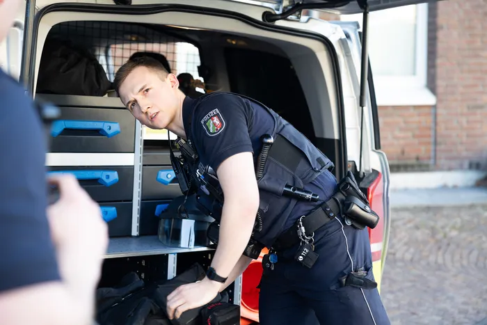 Ein Polizist in Uniform steht lächelnd neben einem geöffneten Transporter und nimmt Ausrüstung heraus.