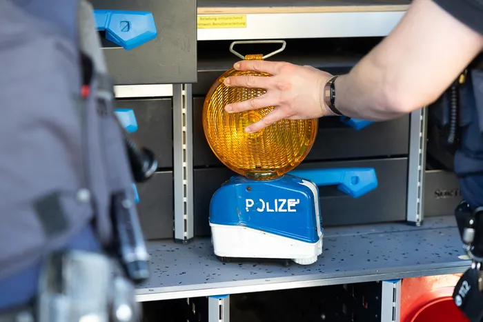 Eine Hand greift nach einem orangefarbenen Warnlicht auf einem blauen Gerät mit der Aufschrift „POLIZEI“ in einem Fahrzeuginnenraum.