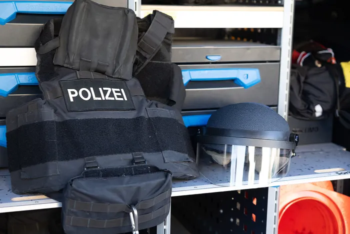 Schwarze Schutzweste mit dem Aufdruck „POLIZEI“ und ein Schutzhelm stehen auf einem Regal in einem Einsatzfahrzeug.
