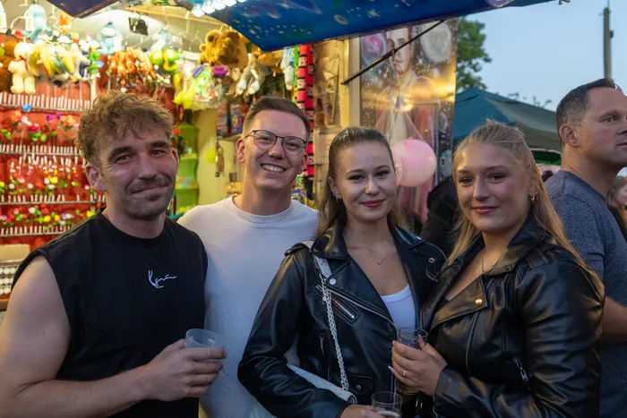 Vier lächelnde junge Menschen posieren vor einem Stand mit bunten Spielzeugen bei der Q-Stall-Party in Schalksmühle.