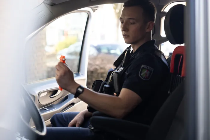 Ein Polizist im Streifenwagen hält einen Atemalkoholtest in die Hand. Er sitzt am Fahrersitz und blickt konzentriert auf das Gerät.