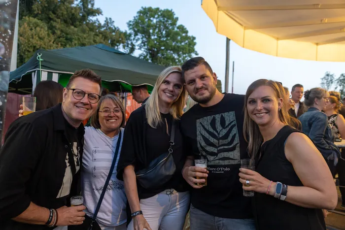 Eine Gruppe von fünf lächelnden Personen posiert mit Getränken bei der Q-Stall-Party im Freien.