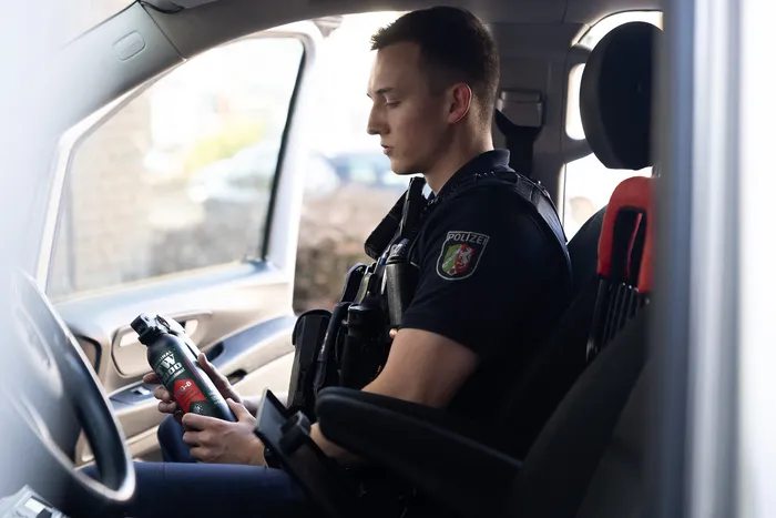 Ein Polizist im Streifenwagen hält eine Dose mit einem Getränk in der Hand und blickt nachdenklich aus dem Fenster.