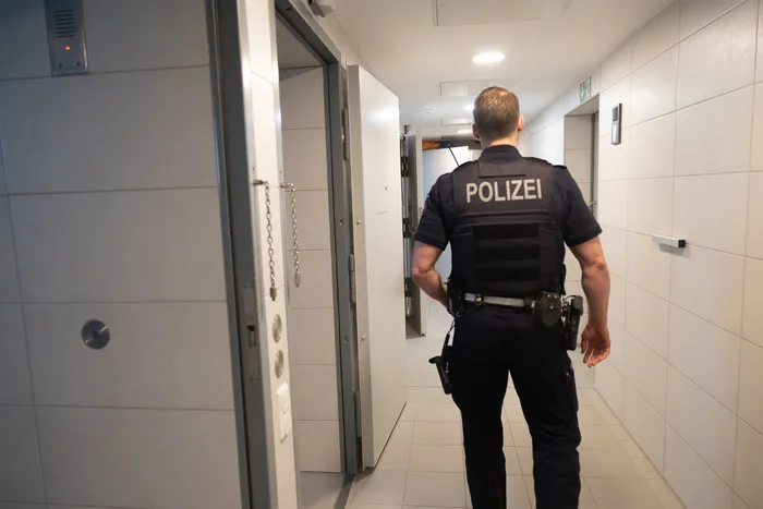 Polizist mit Schutzweste und Dienstausrüstung geht in einem Flur einer öffentlichen Einrichtung, vermutlich einer Schule, weiter.