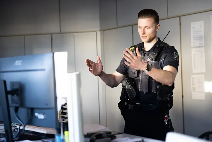 Ein Polizist erklärt mit Handgesten etwas vor einem Computerbildschirm in einem Büro.