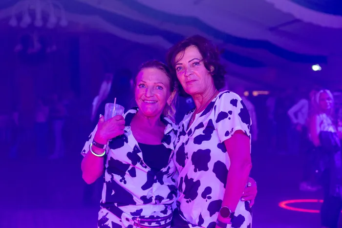 Zwei lächelnde Frauen in schwarz-weiß gemusterten Outfits mit Kuhprint posieren bei einer Party unter lila Licht.