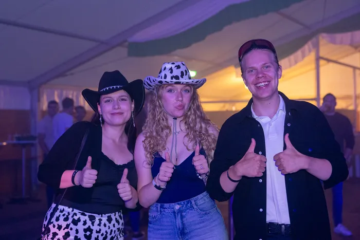 Drei junge Menschen geben bei einer Party in einem Zelt Daumen hoch, zwei davon tragen Cowboyhüte.