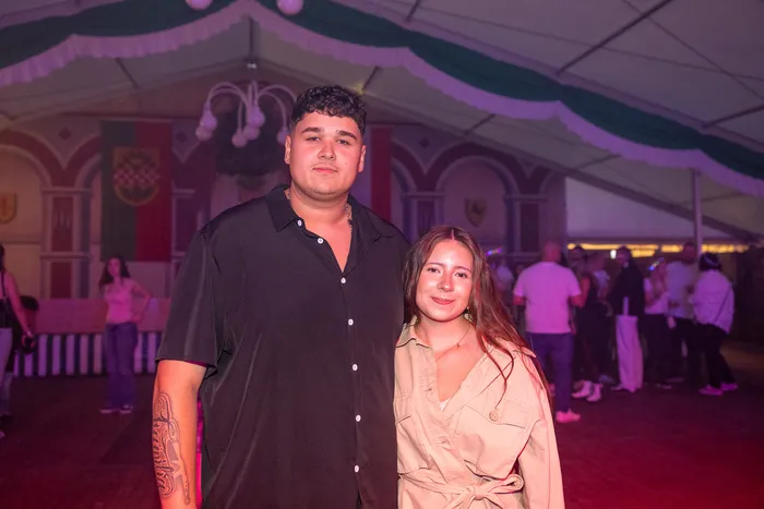 Ein junger Mann in einem schwarzen Hemd und eine junge Frau in einem beigen Hemd posieren bei einer Party in einem Festzelt.