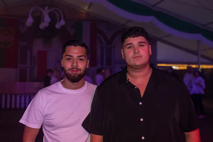 Zwei junge Männer in einem weißen T-Shirt und einem schwarzen Hemd blicken bei der Q-Stall-Party in die Kamera.