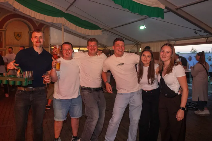 Eine Gruppe lächelnder junger Menschen posiert mit Getränken unter einem Festzelt bei der Q-Stall-Party.