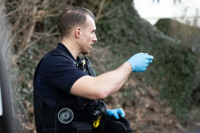 Ein Polizist mit Handschuhen deutet an einem Einsatzort auf etwas in der Ferne.