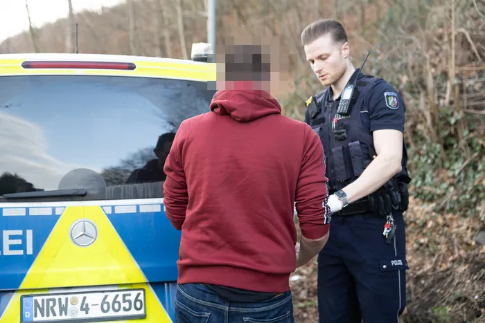 Polizist kontrolliert eine Person am Straßenrand, während ein weiteres Fahrzeug im Hintergrund steht.