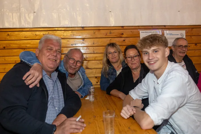 Sechs Personen sitzen lächelnd an einem Holztisch während der Q-Stall-Party in Schalksmühle.
